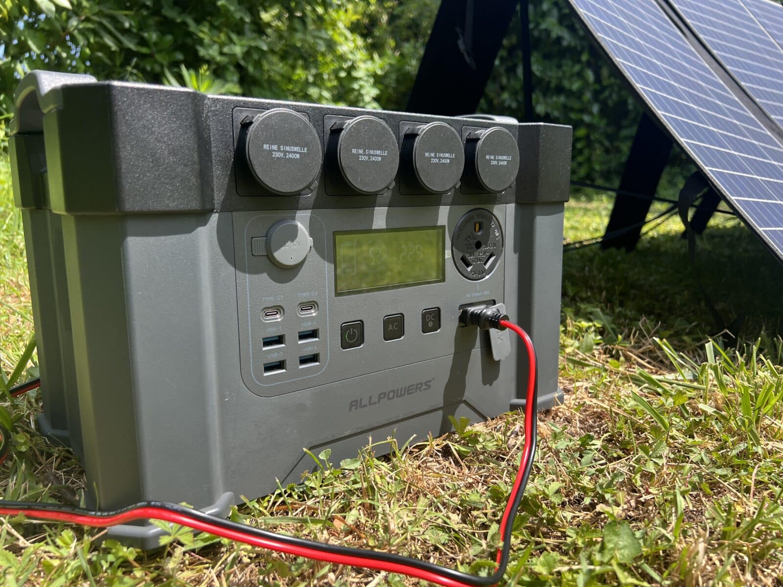 Vue de la batterie ALLPOWERS S2000 Pro posée sur l'herbe, connectée à un panneau solaire pour la recharge en plein air