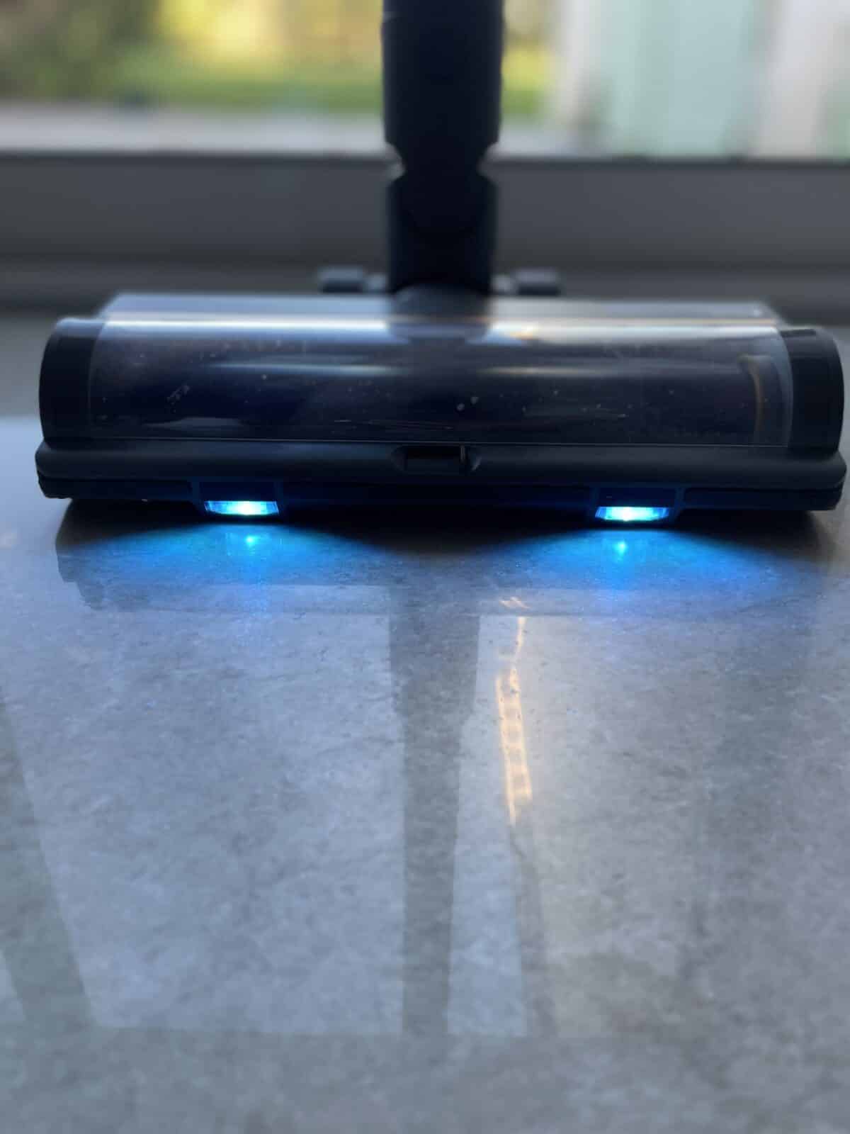 Fonctionnalité de la lumière LED bleue du Dreame R20 éclairant la poussière sur le sol pour une meilleure visibilité