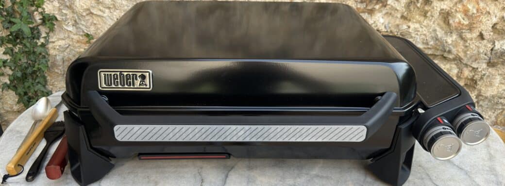 Plancha Weber allumée, prête à cuisiner en extérieur avec des ustensiles