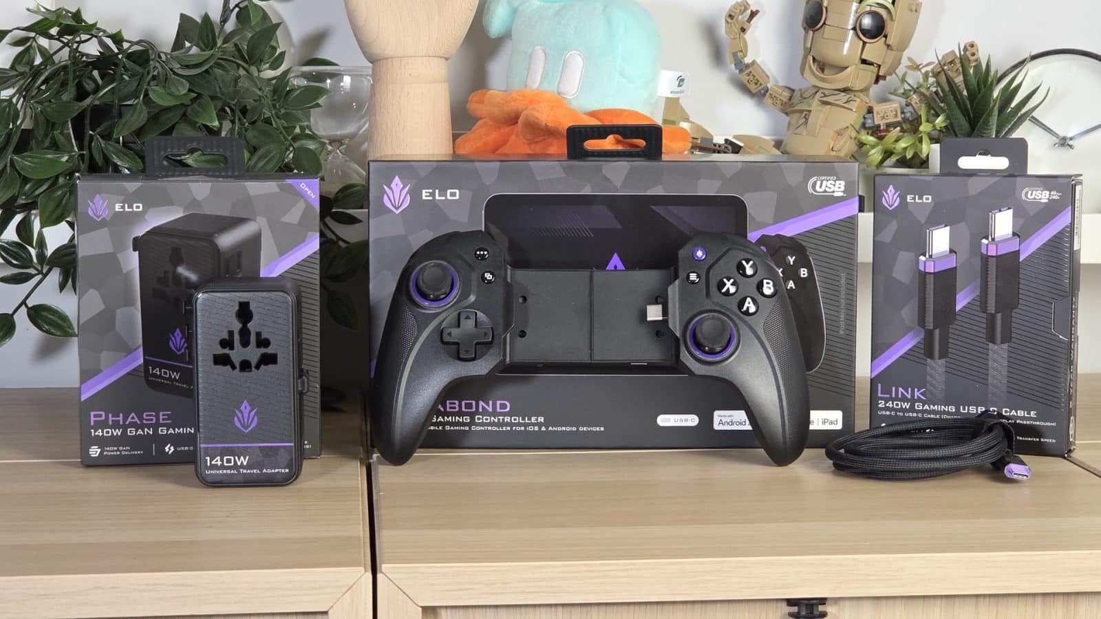 Les trois accessoires Elo alignés : manette Vagabond, chargeur Phase et câble Link dans leurs boîtes