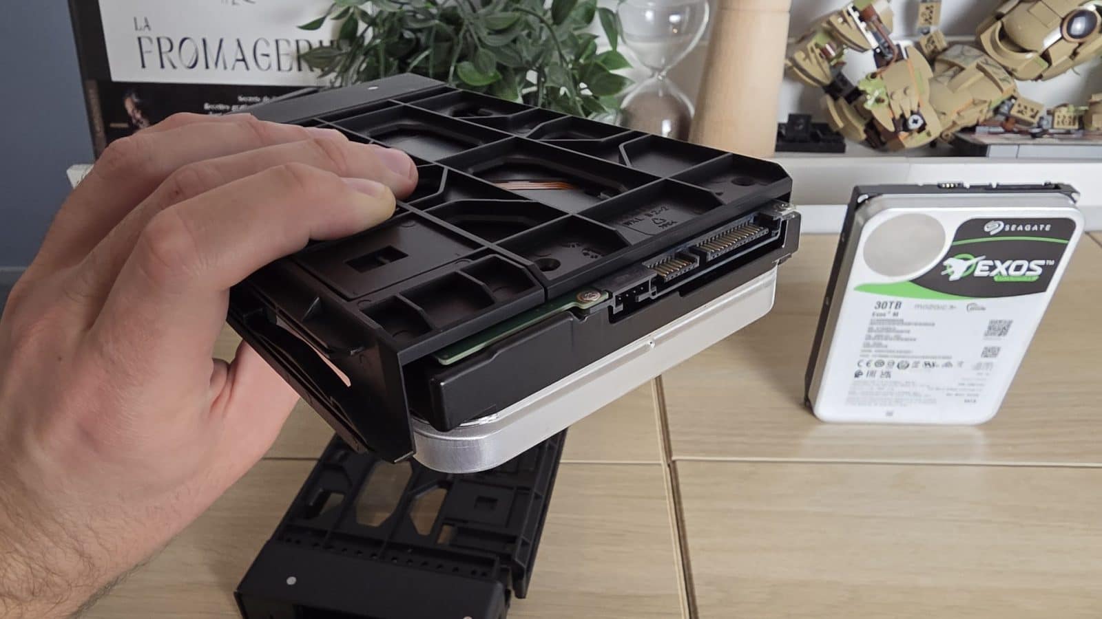 Disque dur Seagate Exos M 30 To tenu à la main au-dessus d'un tiroir de NAS, second disque à côté